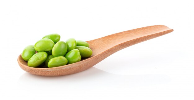 Green soybeans in wood spoon on white table