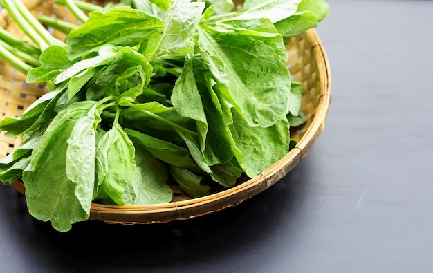 Green spinach in bamboo basket on dark background.