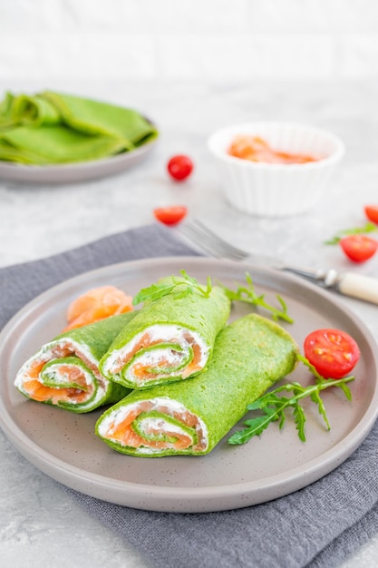 Green spinach crepes or pancakes with smoked salmon and soft cheese on a plate Copy space