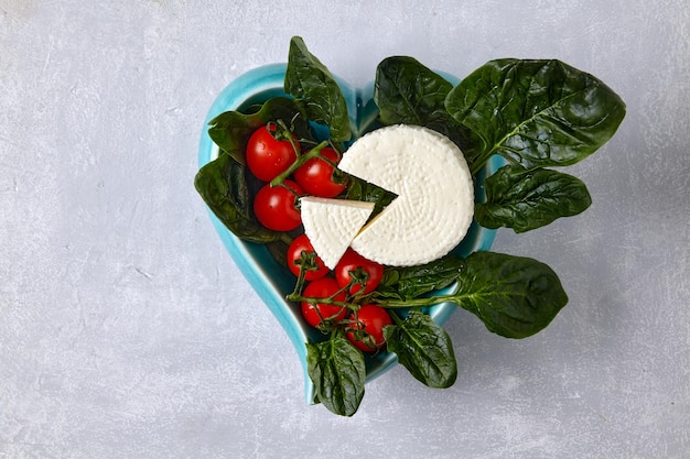 Green spinach leaves and mozzarella curd cheese on a dark plate on a light concrete table