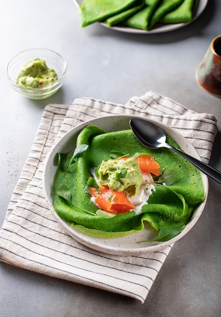 Green spinach pancakes with salmon and avocado on a gray concrete surface. tasty breakfast. vertical image