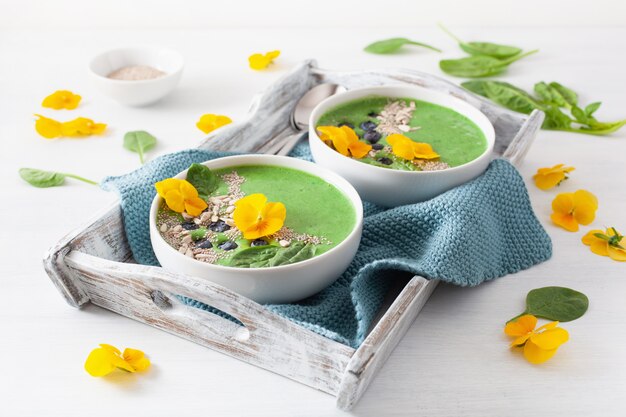 Green spinach smoothie bowl with blueberry, chia seed and edible pansy flowers