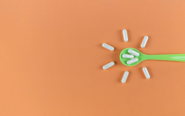 Photo green spoon and white capsules on a orange backdrop with copy space.