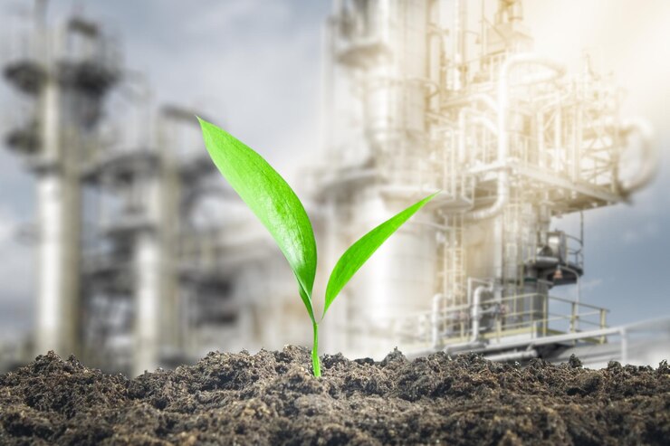 A green sprout grows out of the ground against the background of an oil and gas processing plant Concern for the environment