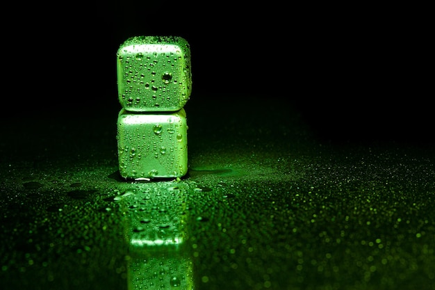 Green stainless steel cubes simulating ice for cooling drinks on a black surface with a reflection.