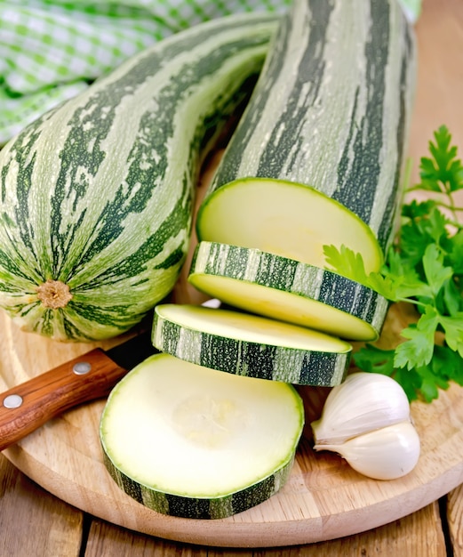 Green striped zucchini, garlic, parsley, napkin, knife on a wooden board