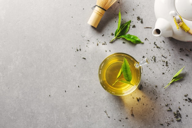 Green tea brewed in cup with tea leaves on table. Closeup.