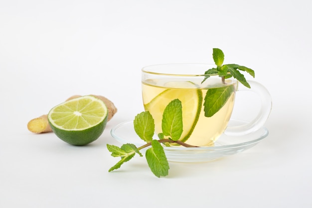 Green tea in a glass cup, ginger, lime and mint on a white table. Healthy food