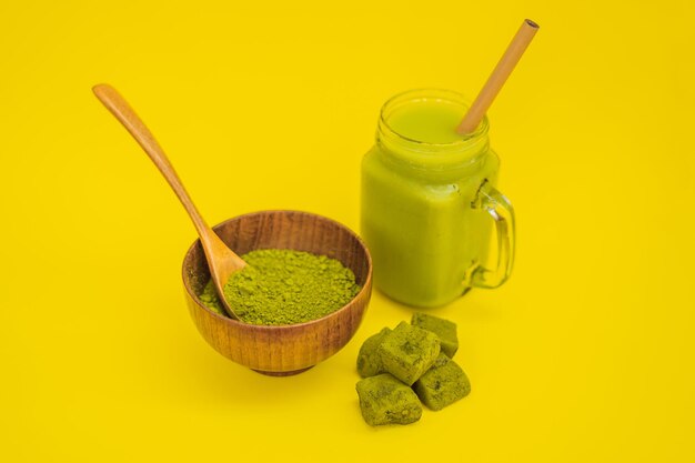 Green tea latte with ice in mason jar matcha powder and candy made of matcha on yellow background