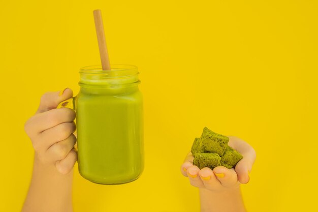 Green tea latte with ice in mason jar matcha powder and candy made of matcha on yellow background