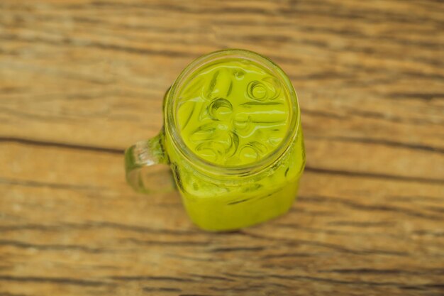 Foto tè verde latte con ghiaccio in barattolo di vetro e paglia su sfondo di legno tè freddo matcha latte fatto in casa con latte zero rifiuti