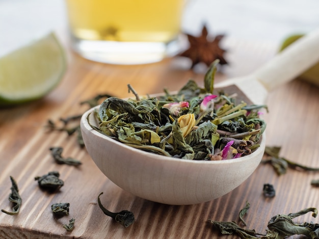 Green tea leaves in wooden spoon with lime slices on wooden background or surface, close-up