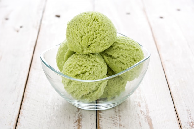 Green tea matcha ice cream scoops in crystal bowl on white wooden table