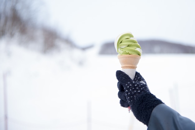 Green Tea (Matcha) and Vanilla Flavor Ice Cream Soft Cream in crispy cone holding in hand with snow 