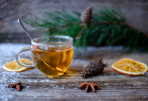 Green tea with a glass Cup on a wooden table with pine branches, dried oranges , pine cones, anise stars and snow