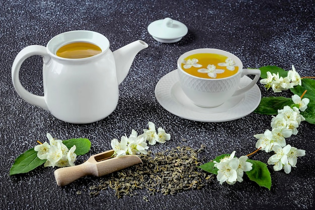 Green tea with jasmine in a white cup and teapot on a dark background wooden spoon