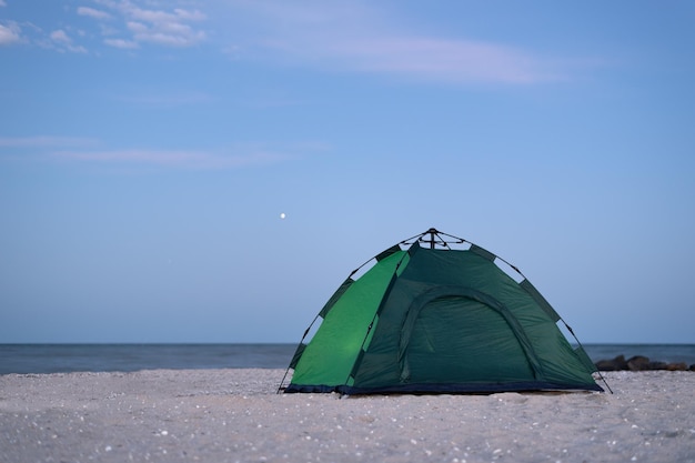 Green tent against blue sky and sea background Camping on beach Evening