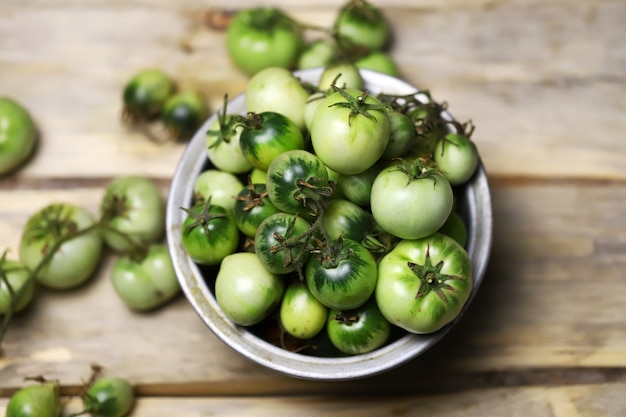 Green tomatoes in a bowl on a wooden surface.