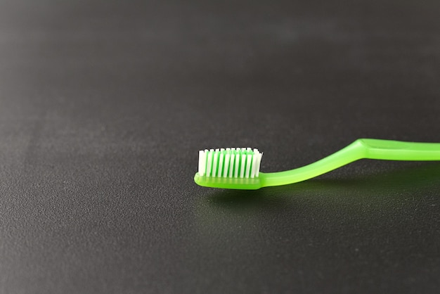 A green toothbrush with a white bristles on a black surface.