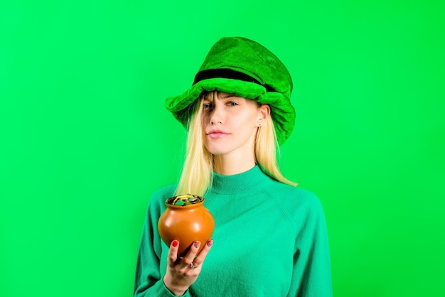 Una ragazza bionda con cappello a cilindro verde in costume da folletto tiene un barattolo con una borsa da folletto d'oro con verde dorato