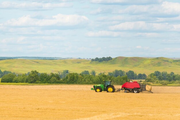 Green tractor on the yellow agricultural field on the background of hills and blue sky