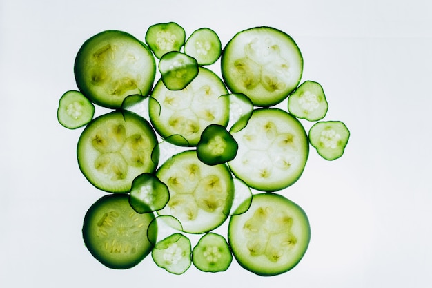 明るい白い光のクローズアップの背景にキュウリの緑の半透明のスライス。野菜の透明なディスク。マクロの万華鏡パターンのテクスチャ