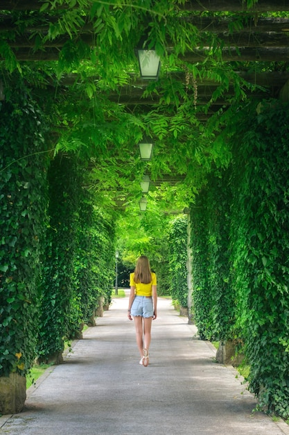 写真 緑の木の路地とスロベニアの夏の美しい咲く公園で幸せな若い女性 春の緑の葉のつる植物を持つ女の子の小道の風景 ライフ スタイルの背景 自然 木のトンネル