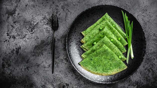 Green vegan crepes with spinach on dark background. Healthy breakfast, vegetarian food, banner, menu recipe place for text, top view.