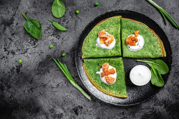 Green vegan crepes with spinach, smoked salmon and yogurt sauce, Healthy breakfast, vegetarian food, top view.