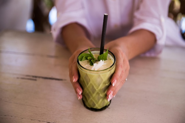 Green vegan healthy smoothie with mint in glass in female hands