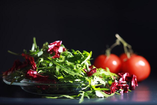 Insalata verde vegana di mix di foglie verdi e verdure. foglie di rucola fresca in uno scolapasta. sfondo nero.