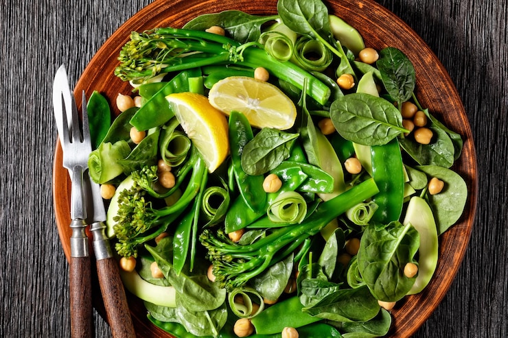 Photo green vegetable salad of sauteed tenderstem broccoli mangetout avocado cucumber chickpeas baby spinach with olive oil dressing served on a brown clay plate on a dark table closeup top view
