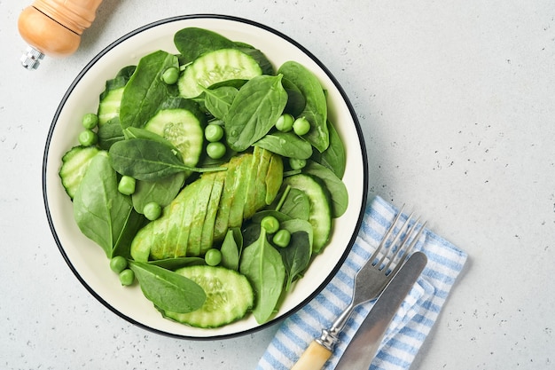 Green vegetable salad with spinach, avocado, green peas and olive oil in bowl on light gray slate