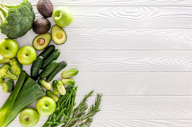 Green vegetables avocado broccoli beans leek and fresh apple on white wooden