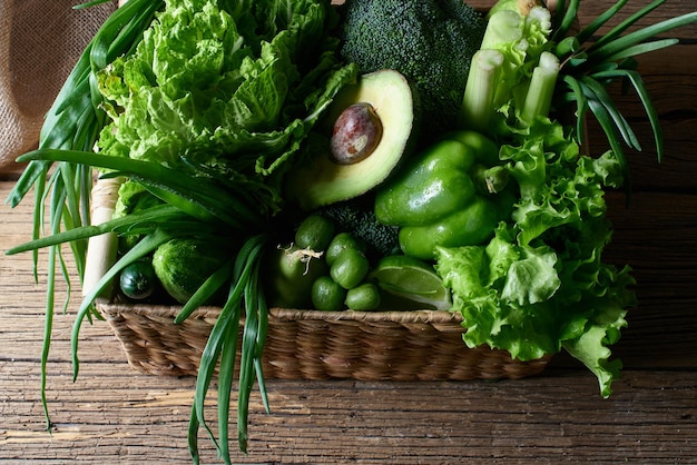 緑の野菜と果物と緑の木製の背景に茶色の籐のバスケット。健康的な食事の概念