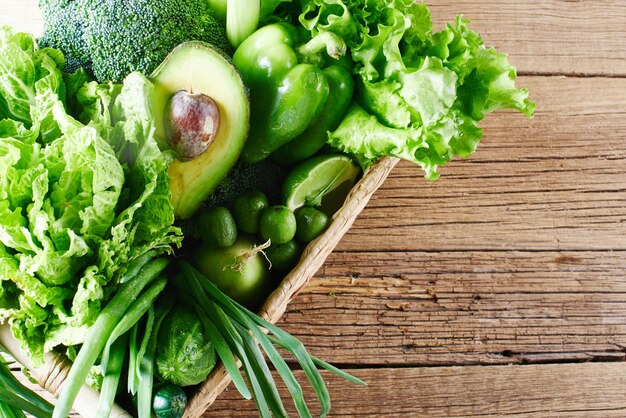 나무 배경에 있는 갈색 고리버들 바구니에 녹색 야채와 과일, 채소. 건강한 식생활 개념