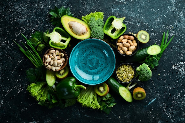 Green vegetables fruits and nuts avocado broccoli pistachios\
parsley celery cucumber and kiwi top view rustic style