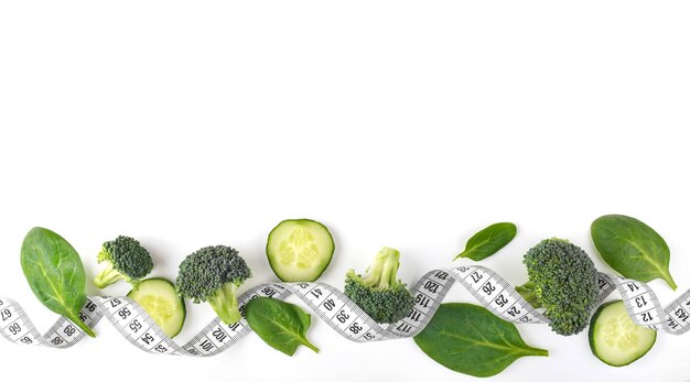 Зеленые овощи и измерительная лента на белом фоне Концепция здорового образа жизни Концепция диеты