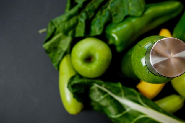 Green vegetables and smoothies in a plastic bottle on black background Healthy concept Top view Space for text
