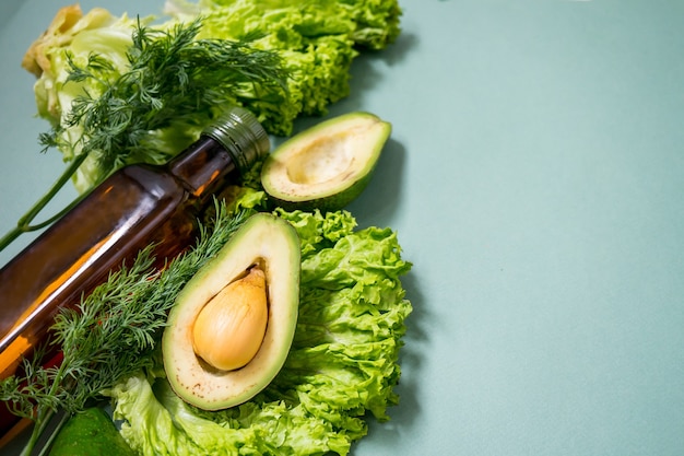 Green vegetables with glass boutle of oil on a green background Avocado Romano salad greens Top view No plastic Healthy diet concept