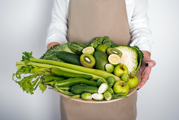 Green vegetables on wooden plate on white background