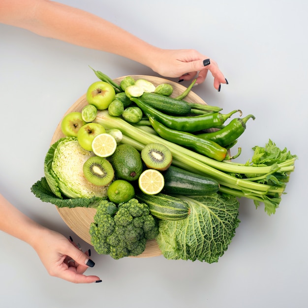 Green vegetables on wooden plate on white background