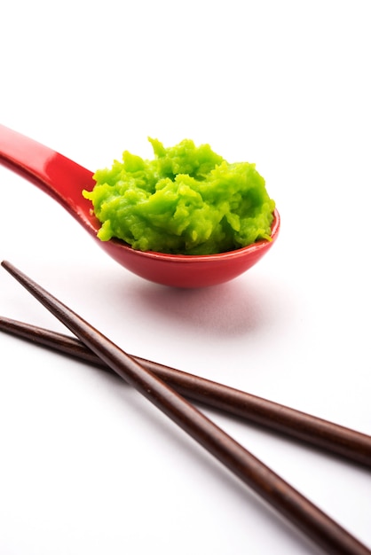 Green wasabi sauce or paste in bowl, with chopsticks or spoon over plain colourful background. selective focus