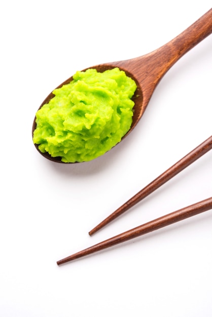 Green wasabi sauce or paste in bowl, with chopsticks or spoon over plain colourful background. selective focus