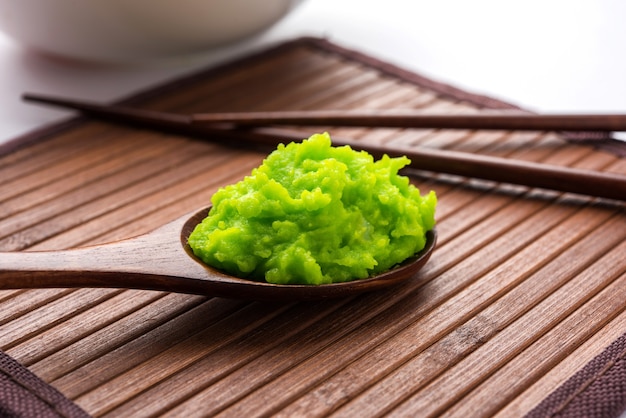 Photo green wasabi sauce or paste in bowl, with chopsticks or spoon over plain colourful background. selective focus