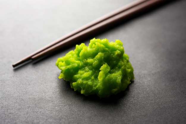 Foto salsa o pasta di wasabi verde in una ciotola, con le bacchette o un cucchiaio su uno sfondo colorato. messa a fuoco selettiva