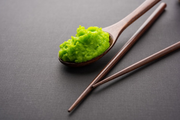 Green wasabi sauce or paste in bowl, with chopsticks or spoon over plain colourful background. selective focus