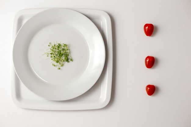 Foto crescione verde su un piatto bianco rotondo e una vista laterale di tre pomodori ciliegia rossi freschi in una fila