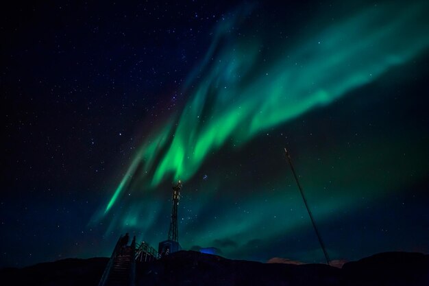 山とヌーク グリーンランドの電波塔の上に星が輝くオーロラの緑の波