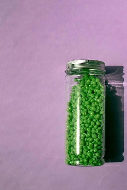 Green wax for depilation in granules on a purple background jar with wax on isolated background